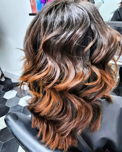 Dark brown hair blending into copper ends, styled in glossy waves